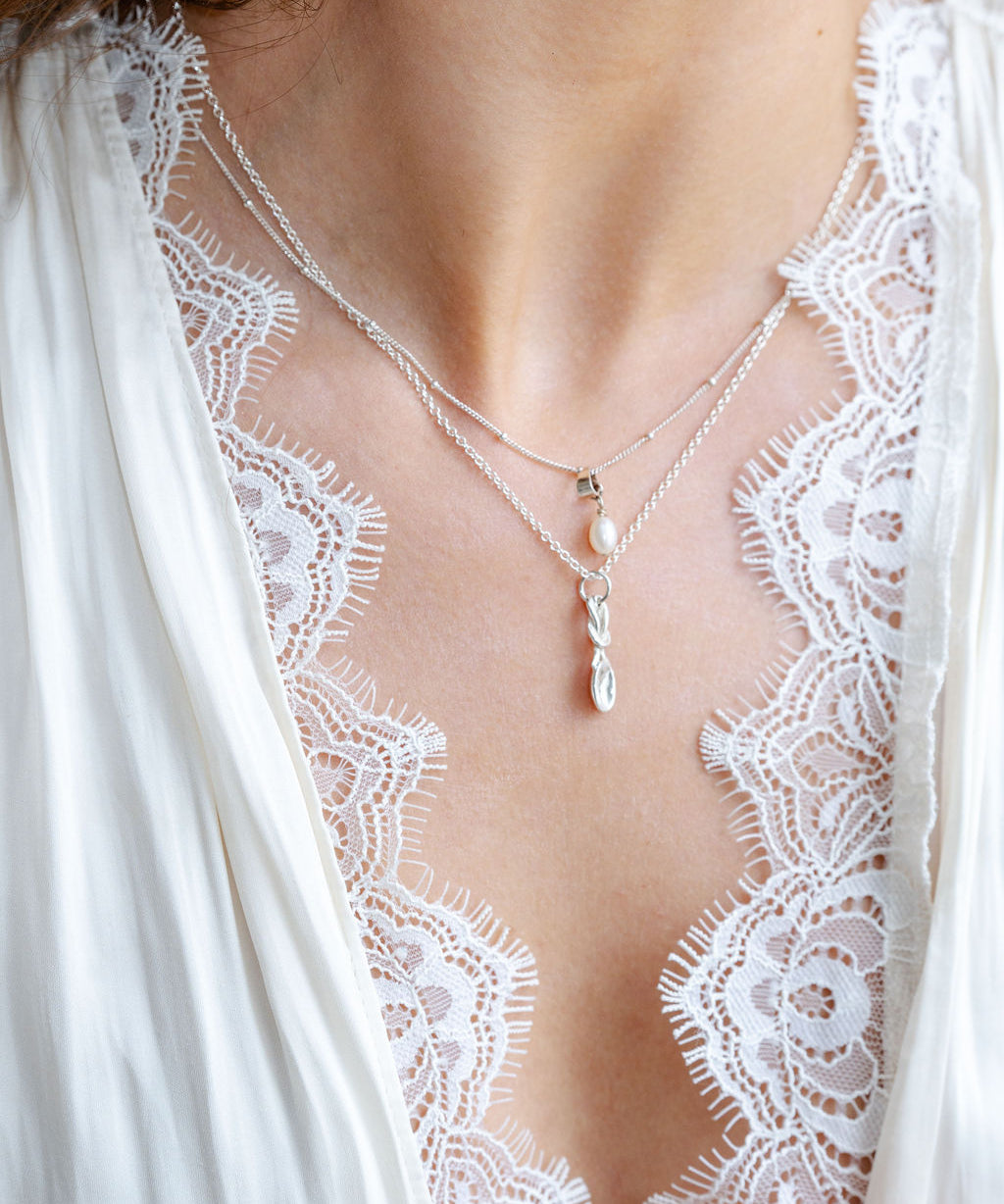 Close-up of a person wearing a delicate necklace with a white lace garment.