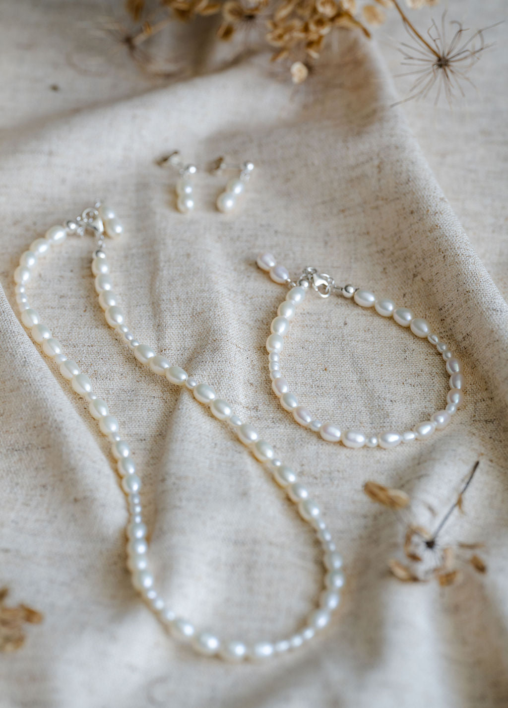 Pearl necklace, earrings  and bracelet set on a textured beige fabric background
