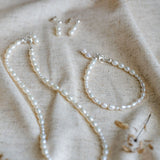 Pearl necklace, earrings  and bracelet set on a textured beige fabric background
