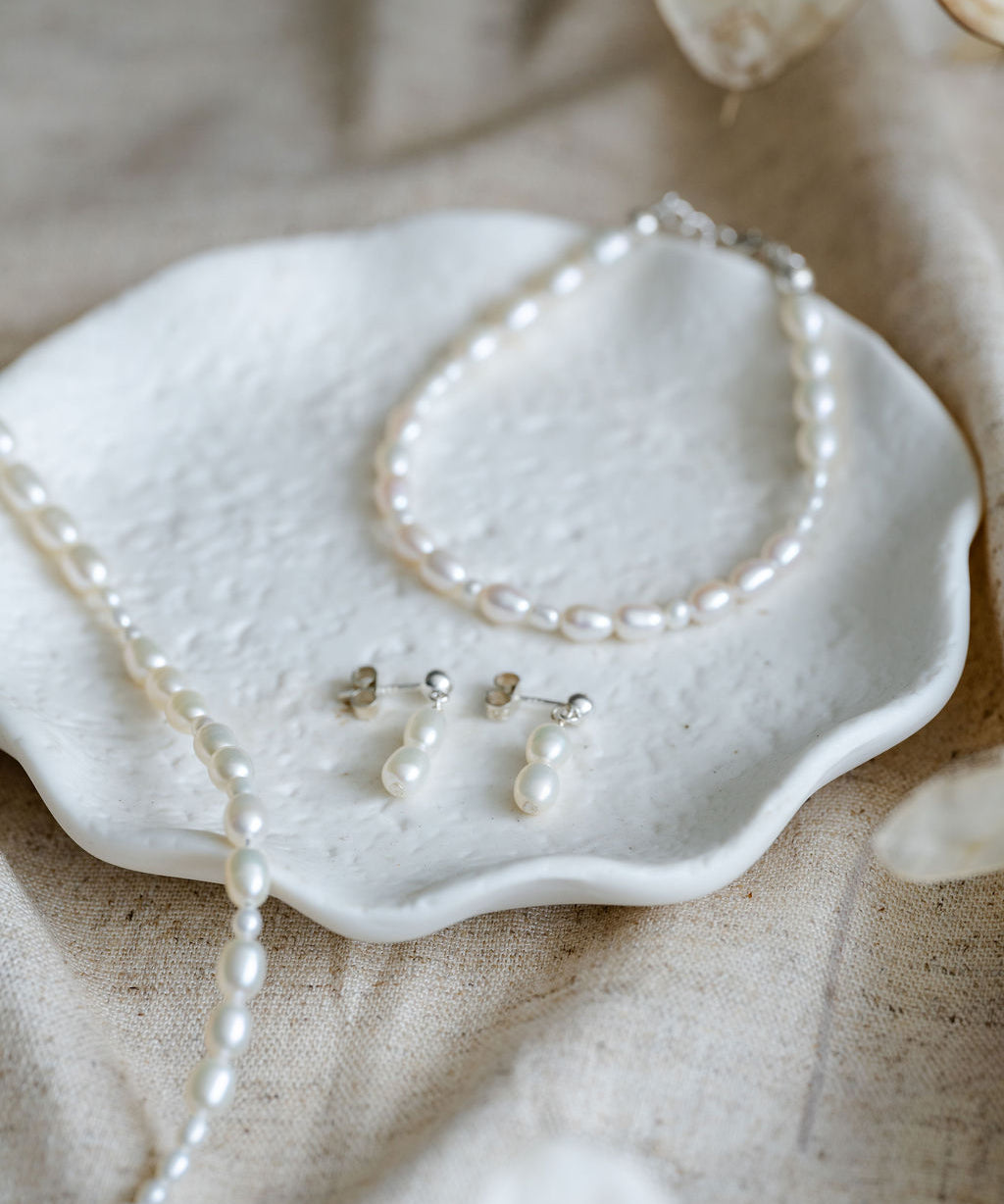 Pearl necklace and earrings  and bracelet on a textured surface