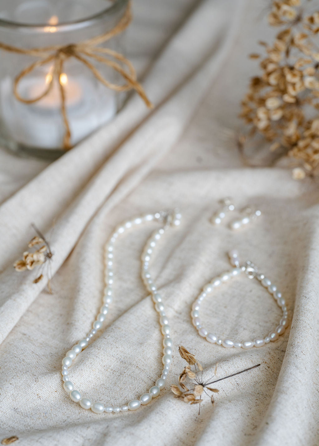 Pearl necklace and bracelet on a textured fabric surface with a candle in the background