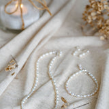 Pearl necklace and bracelet on a textured fabric surface with a candle in the background