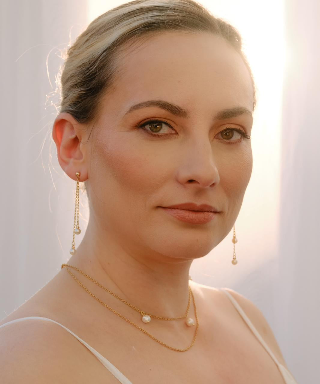 Bride wearing long pearl drop earrings and layered gold necklaces with pearl accents, elegant handmade bridal jewellery set for a modern wedding look.