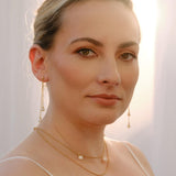 Bride wearing long pearl drop earrings and layered gold necklaces with pearl accents, elegant handmade bridal jewellery set for a modern wedding look.