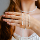 Close-up of a woman's hand wearing multiple silver necklaces with a blurred background.