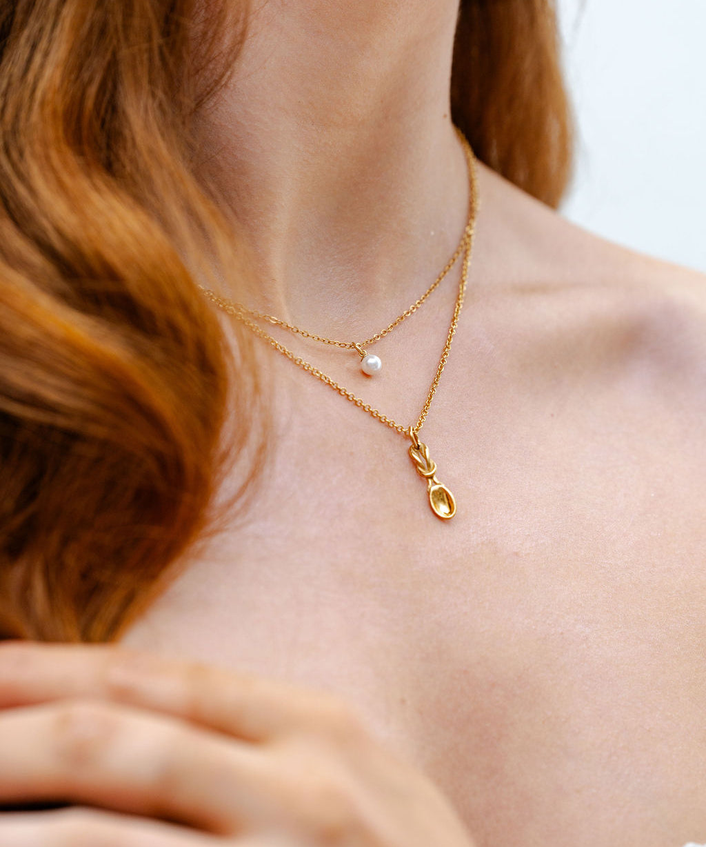 Close-up of a person wearing a gold necklace with a delicate lovespoon pendant.