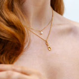 Close-up of a person wearing a gold necklace with a delicate lovespoon pendant.