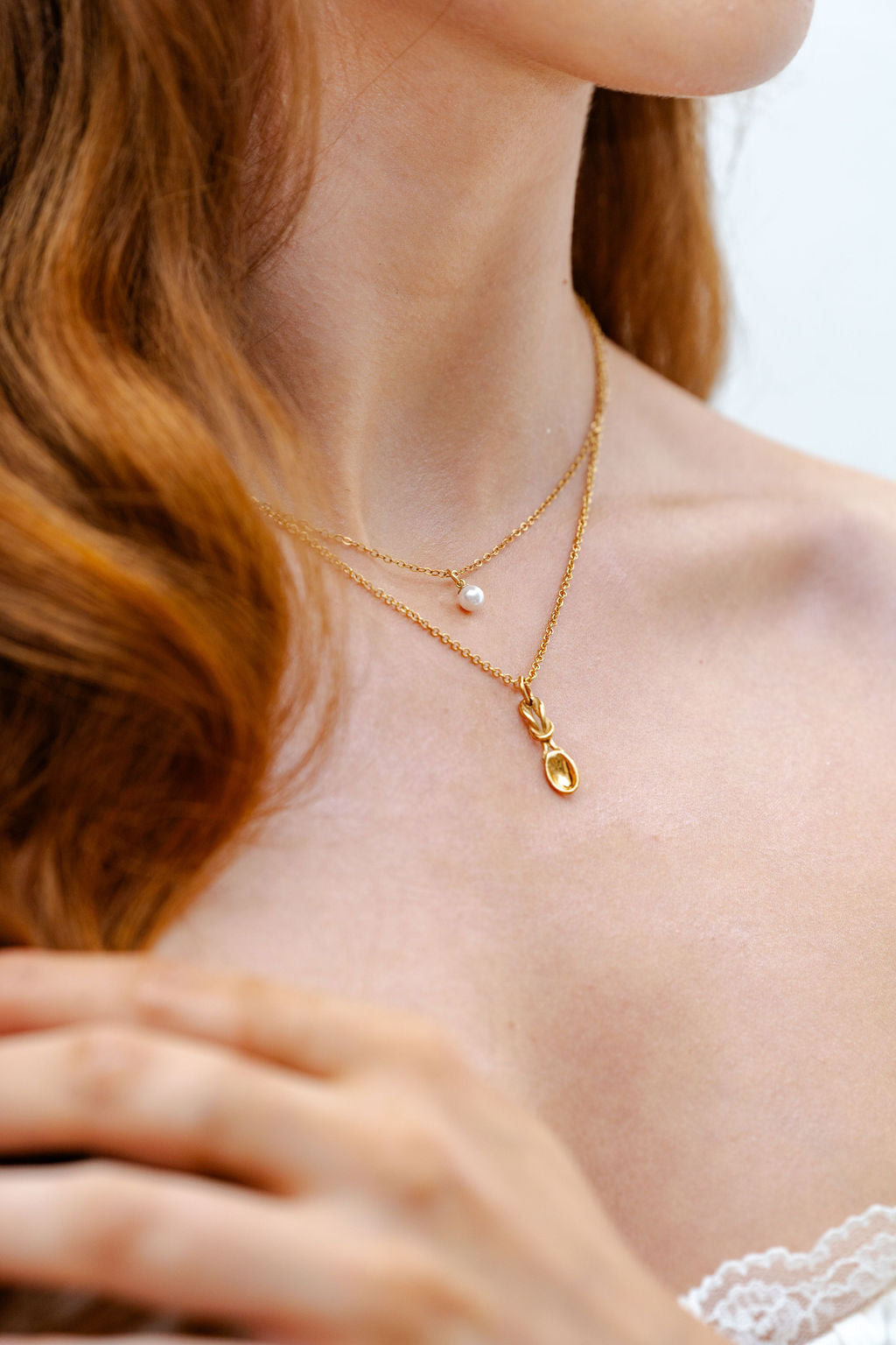 Close-up of a person wearing a gold necklace with a delicate lovespoon pendant.