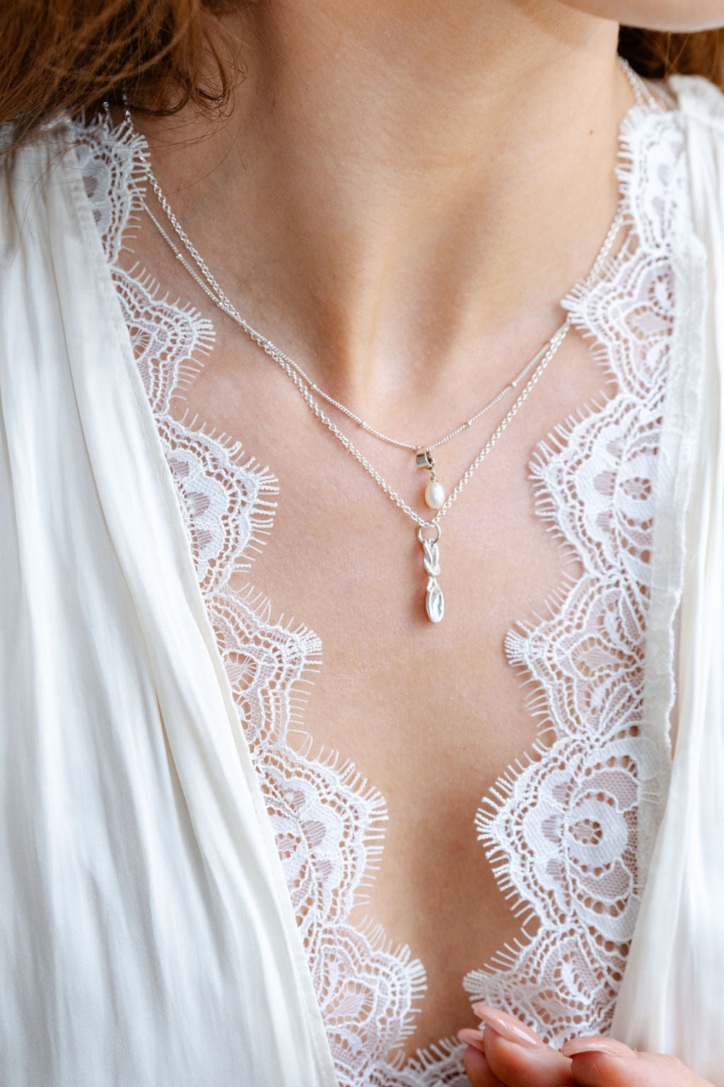Close-up of a person wearing a delicate necklace with a white lace garment.