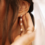 Close-up of a hand adjusting a pearl earring on an ear.