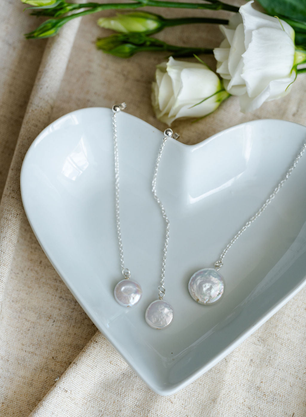 Jewelry set with necklace and earrings on a heart-shaped white dish with flowers in the background.