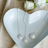 Jewelry set with necklace and earrings on a heart-shaped white dish with flowers in the background.