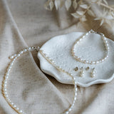 Pearl jewellery set including necklace, bracelet, and earrings on a textured surface with dried leaves.