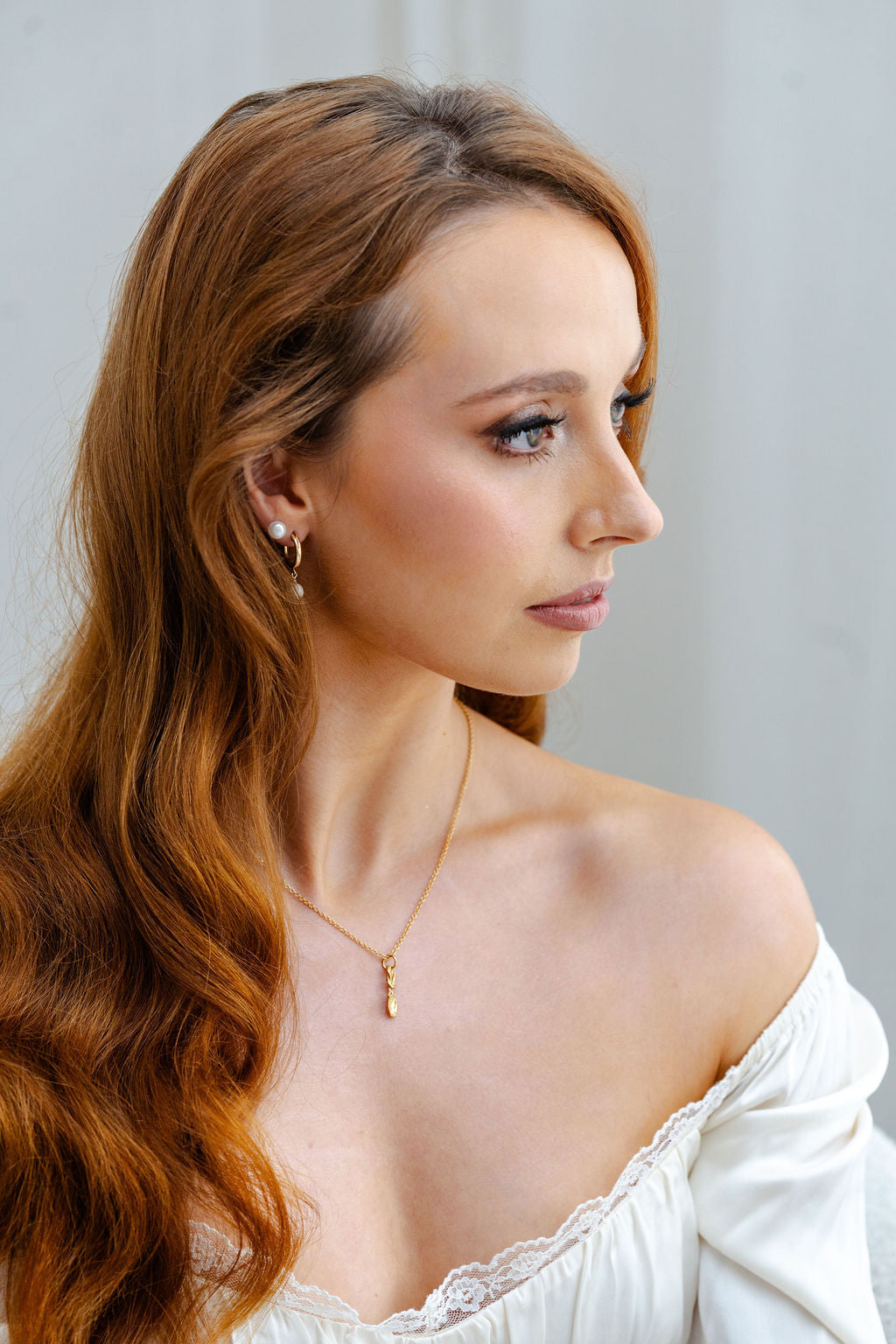 Woman with long wavy hair wearing a gold necklace with lovespoon against a plain background
