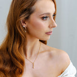 Woman with long wavy hair wearing a gold necklace with lovespoon against a plain background