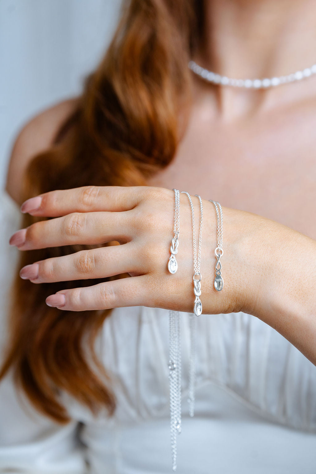 Close-up of a person wearing multiple silver necklaces and bracelets on a plain background