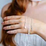 Close-up of a person wearing multiple silver necklaces and bracelets on a plain background