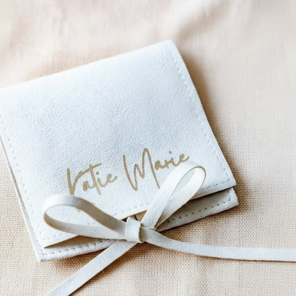 Beige pouch with 'Katie Marie' text tied with a ribbon on a beige background