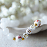 Close-up of a handmade mum bracelet with white gemstone beads and gold letter beads spelling MUM, ideal as a new mum gift or Mother’s Day jewellery.