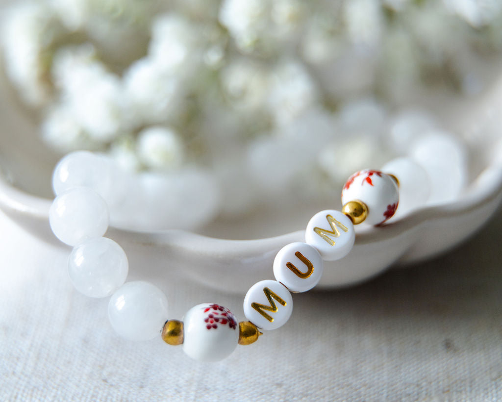 Close-up of a handmade mum bracelet with white gemstone beads and gold letter beads spelling MUM, ideal as a new mum gift or Mother’s Day jewellery.