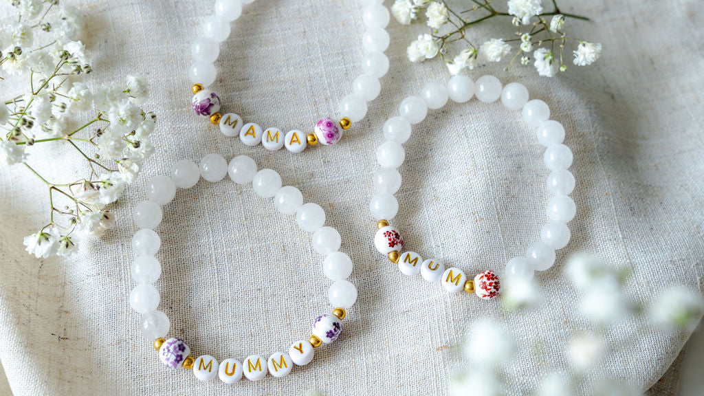 Set of handmade beaded bracelets spelling MUM, MUMMY and MAMA with white gemstone beads and gold lettering, thoughtful handmade jewellery gifts for mums.