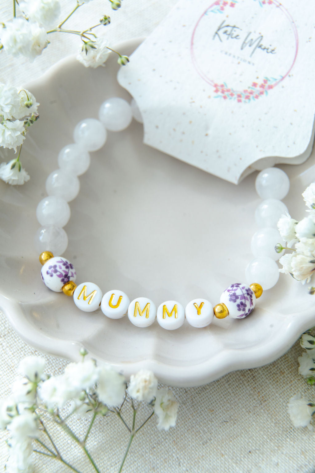 Handmade mummy bracelet with white gemstone beads and gold MUMMY letter beads, displayed in a ceramic dish with Katie Marie Creations tag, meaningful jewellery gift for mums.