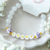 Handmade mummy bracelet with white gemstone beads and gold MUMMY letter beads, displayed in a ceramic dish with Katie Marie Creations tag, meaningful jewellery gift for mums.