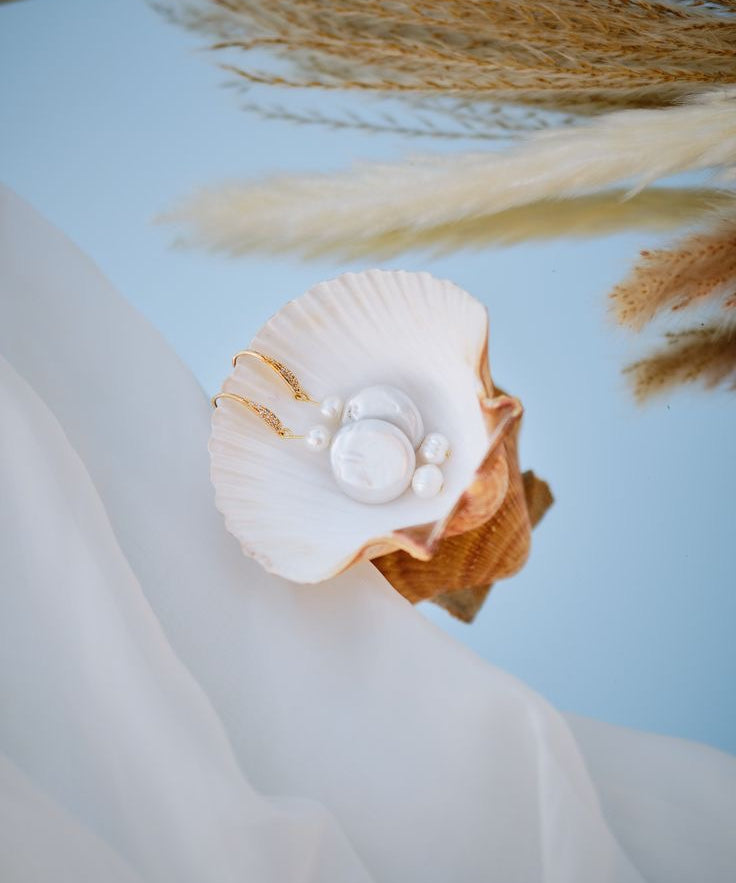 Handmade bridal pearl earrings with gold hooks and layered pearls, styled in a seashell with pampas grass, elegant wedding jewellery for brides.