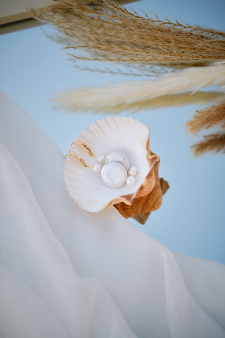 Elegant pearl bridal earrings displayed in a seashell with gold accents, handmade wedding jewellery for brides looking for timeless and romantic pearl accessories.