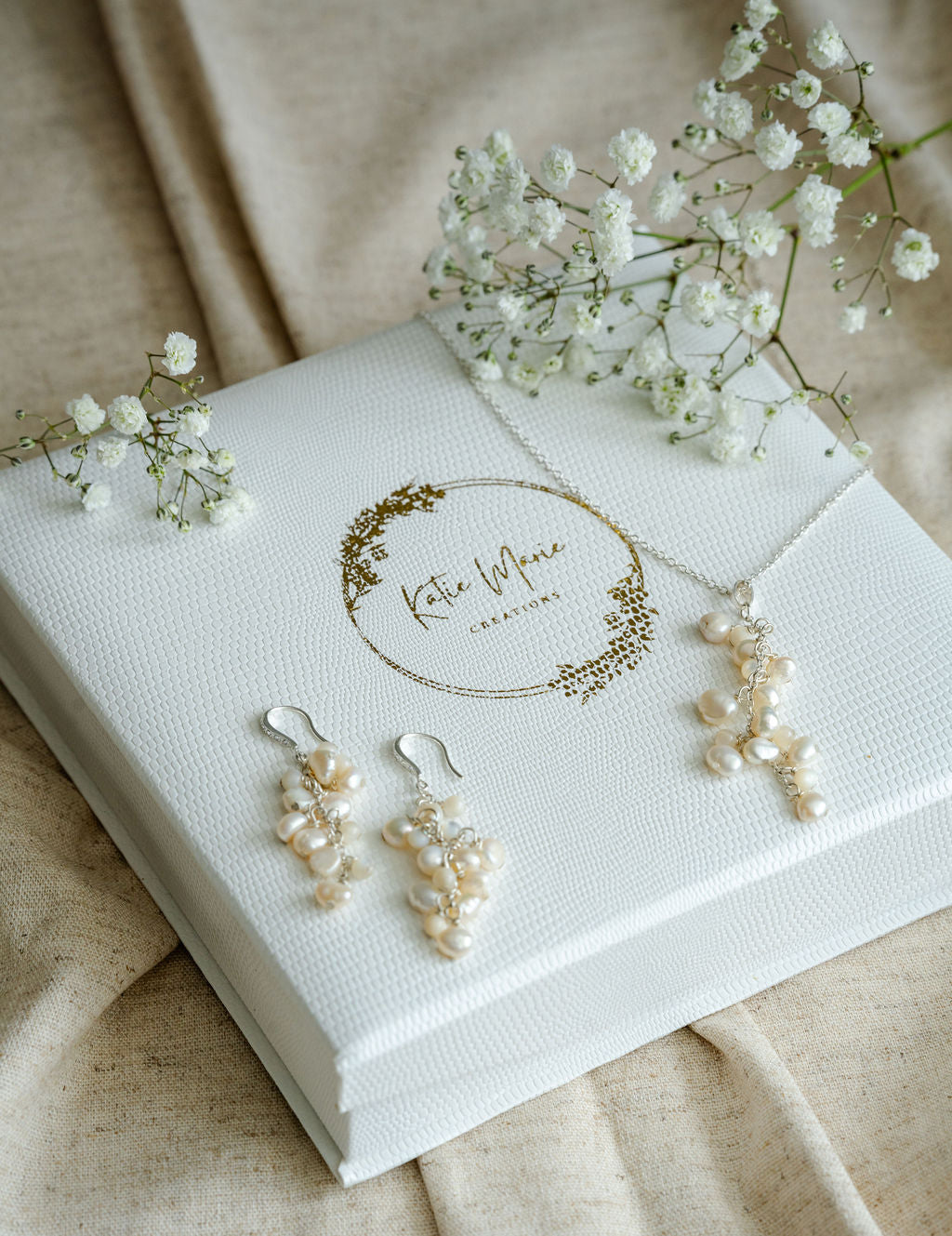 Pearl jewellery set with earrings and necklace on a branded box, surrounded by baby's breath flowers.